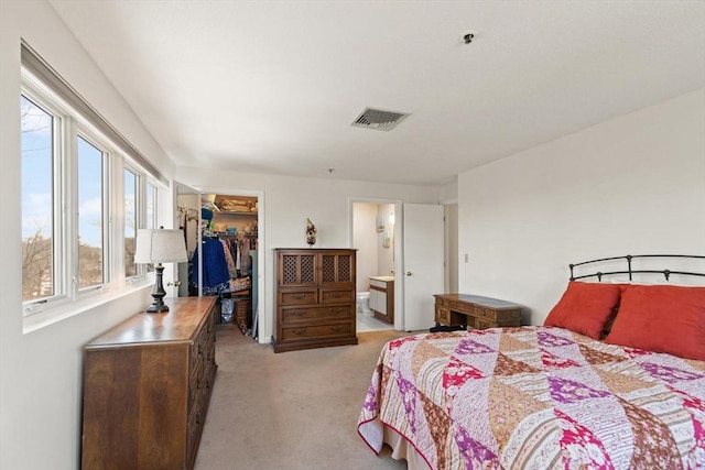 bedroom with connected bathroom, a walk in closet, light colored carpet, and a closet