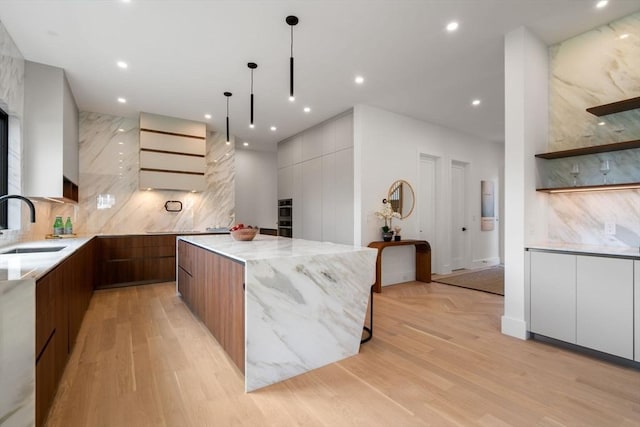 kitchen with backsplash, modern cabinets, a sink, and light stone countertops