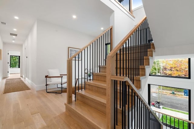 stairs featuring baseboards, visible vents, a towering ceiling, wood finished floors, and recessed lighting