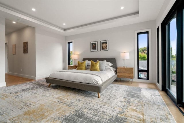 bedroom with a tray ceiling, light wood-style flooring, baseboards, and recessed lighting