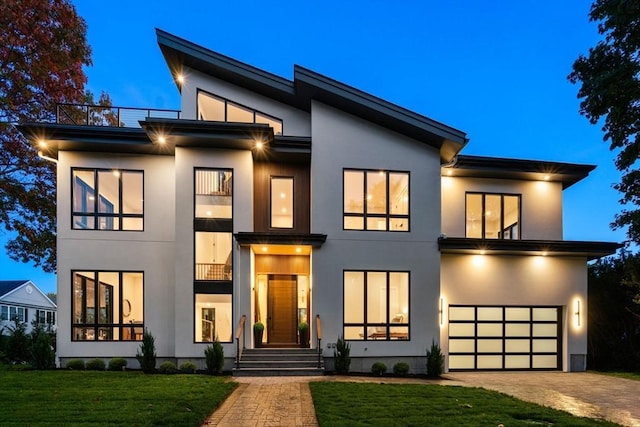 modern home featuring a garage, a front yard, decorative driveway, and stucco siding