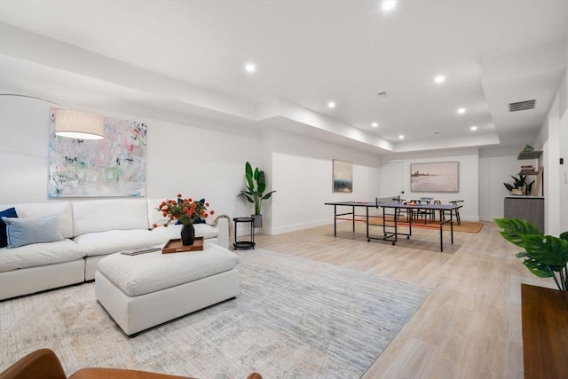 living room with a tray ceiling, light wood finished floors, recessed lighting, visible vents, and baseboards