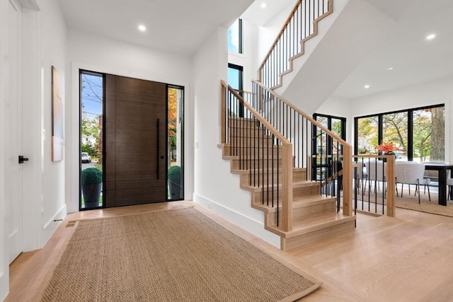 foyer entrance featuring recessed lighting, stairway, a high ceiling, wood finished floors, and baseboards