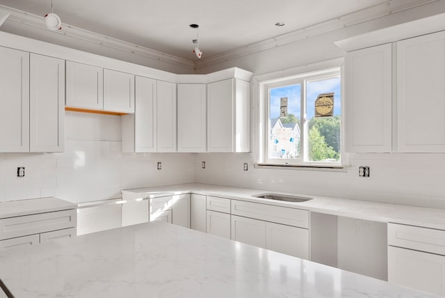 kitchen featuring white cabinets, backsplash, light stone countertops, and crown molding