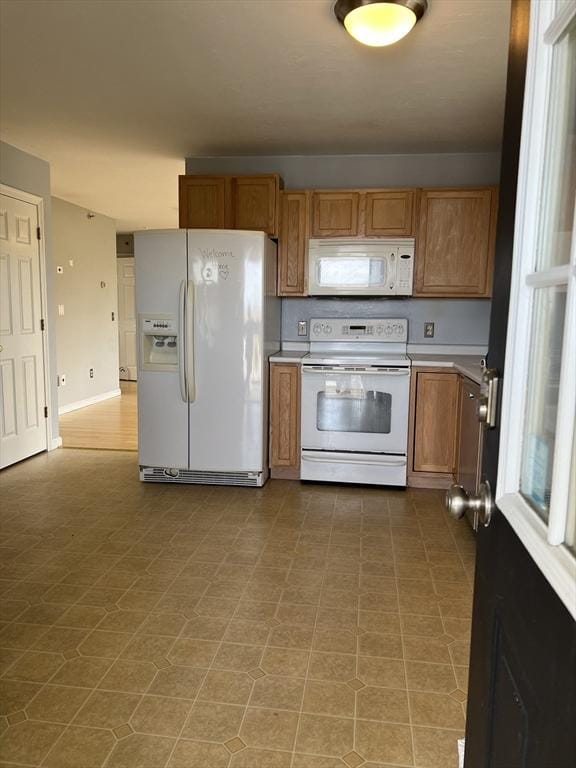 kitchen featuring white appliances, brown cabinetry, light countertops, and light flooring
