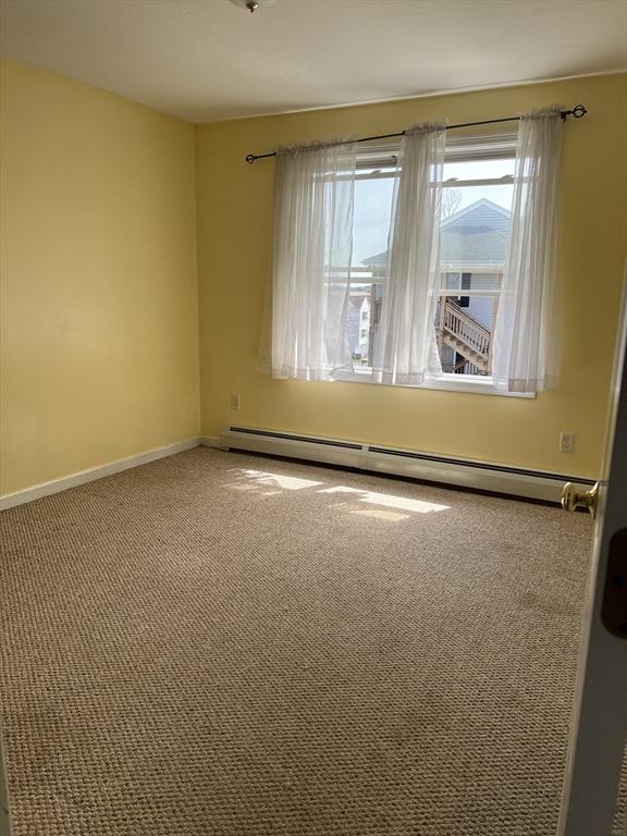 carpeted empty room with a baseboard heating unit and baseboards