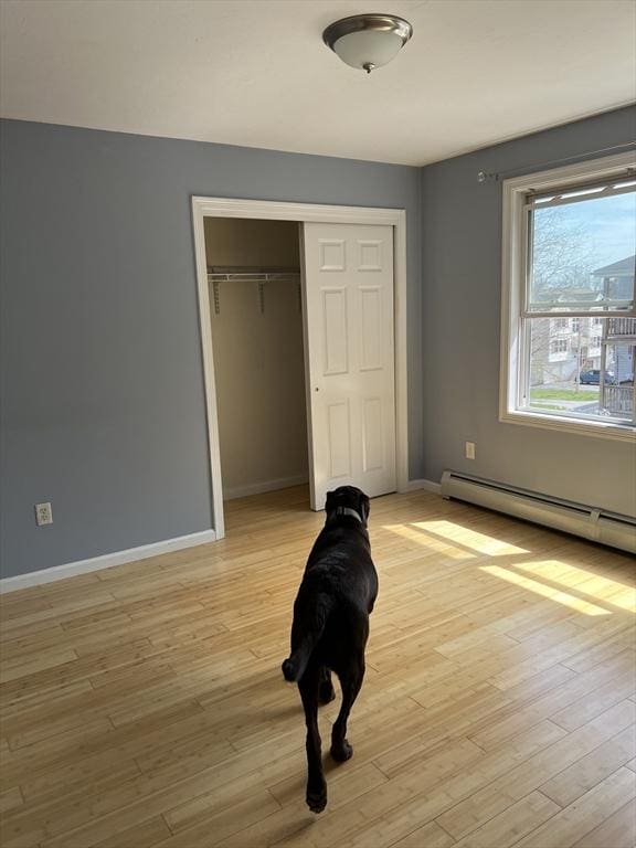 unfurnished bedroom with a closet, baseboards, light wood-style flooring, and a baseboard radiator