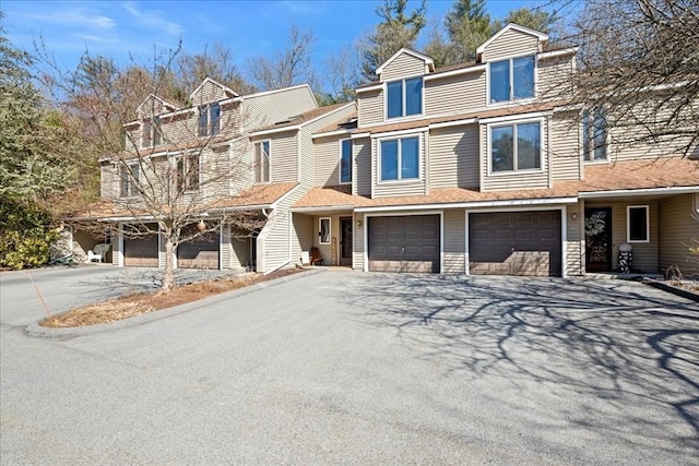 townhome / multi-family property with a garage, driveway, and roof with shingles