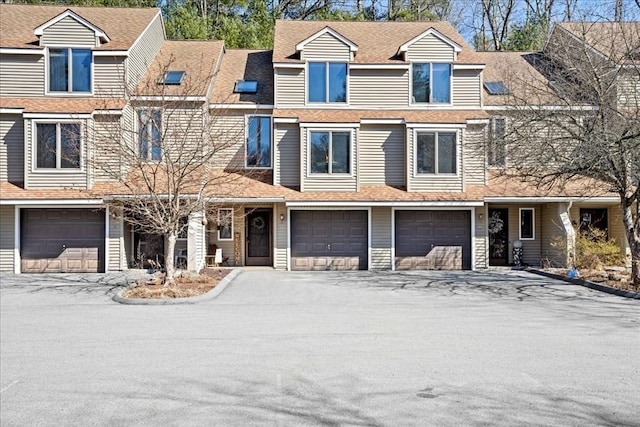 townhome / multi-family property featuring an attached garage, driveway, and roof with shingles