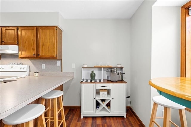 kitchen featuring dark wood finished floors, a breakfast bar, exhaust hood, brown cabinetry, and range