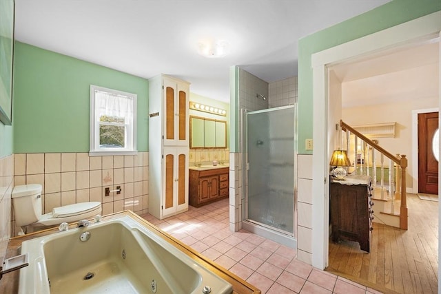 full bathroom featuring toilet, vanity, a tub with jets, tile walls, and a stall shower
