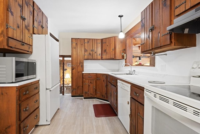 kitchen featuring under cabinet range hood, light countertops, a sink, white appliances, and brown cabinetry