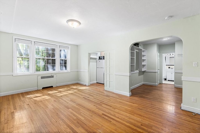 unfurnished room featuring baseboards, arched walkways, radiator, and hardwood / wood-style flooring
