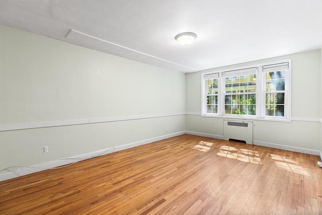 empty room featuring radiator heating unit, baseboards, and light wood-style floors