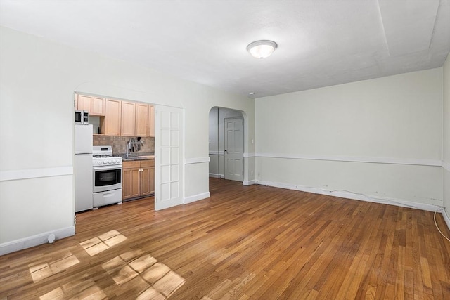 kitchen featuring white gas stove, backsplash, arched walkways, stainless steel microwave, and light wood finished floors