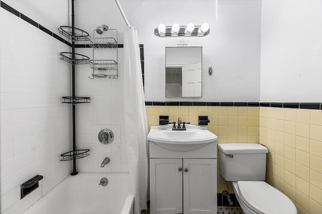 bathroom featuring tile walls, wainscoting, vanity, toilet, and shower / bath combo with shower curtain