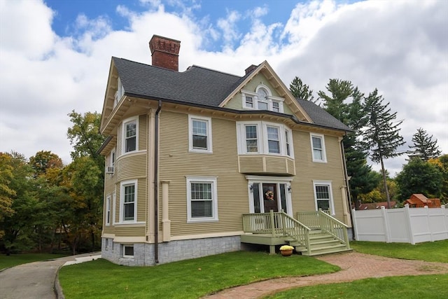 exterior space with fence, a chimney, roof with shingles, and a front lawn