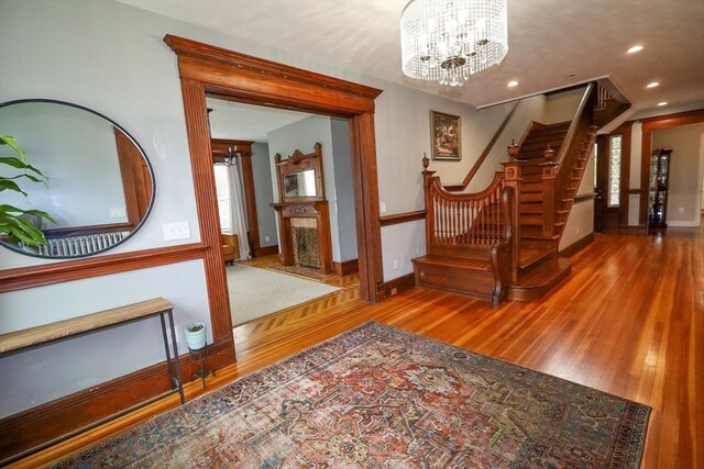 interior space featuring a notable chandelier, a premium fireplace, hardwood / wood-style floors, baseboards, and stairway