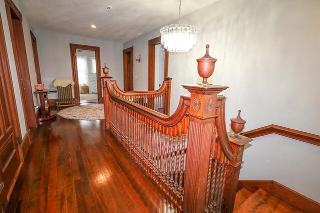 hall featuring an inviting chandelier, wood-type flooring, baseboards, recessed lighting, and an upstairs landing