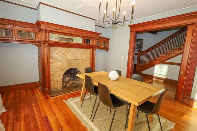 dining space with baseboards, light wood-style floors, stairway, a fireplace with raised hearth, and a notable chandelier