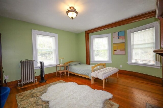 bedroom with radiator heating unit, baseboards, multiple windows, and wood finished floors
