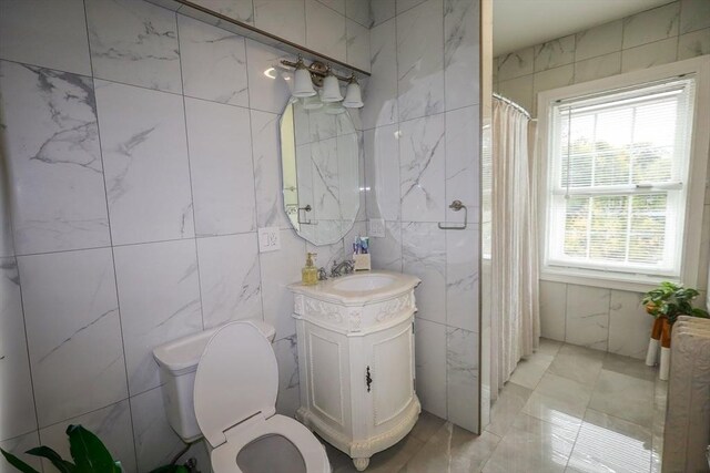 bathroom featuring vanity, marble finish floor, toilet, and tile walls