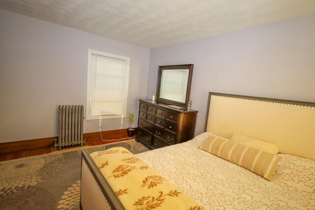 bedroom with baseboards, radiator heating unit, and wood finished floors