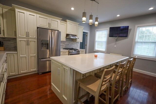 kitchen featuring a healthy amount of sunlight, decorative backsplash, a kitchen island, under cabinet range hood, and stainless steel appliances
