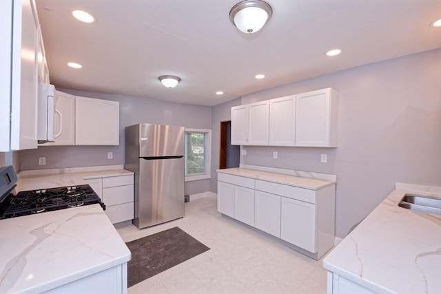 kitchen with freestanding refrigerator, range with gas cooktop, white microwave, light stone counters, and white cabinets
