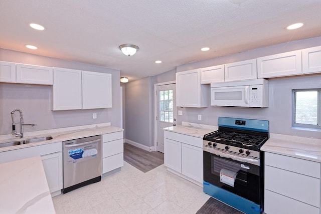 kitchen with appliances with stainless steel finishes, a sink, white cabinets, recessed lighting, and light stone counters