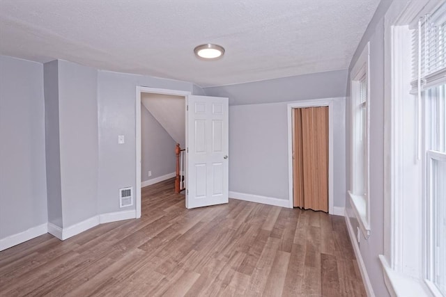 unfurnished bedroom featuring a textured ceiling, wood finished floors, baseboards, a closet, and vaulted ceiling