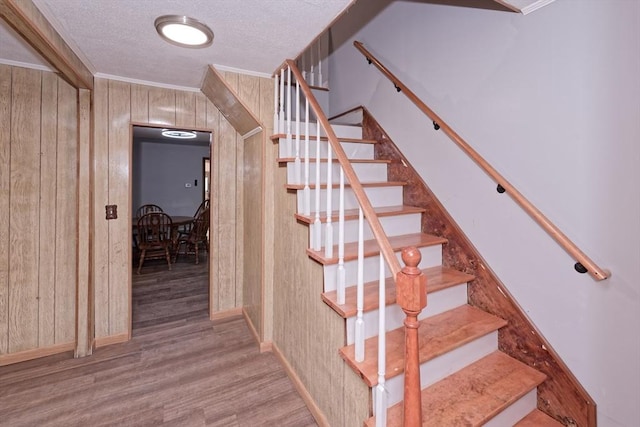 stairway with wood finished floors, wood walls, ornamental molding, a textured ceiling, and baseboards