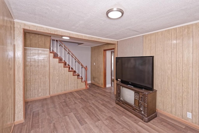 unfurnished living room with stairs, wood finished floors, a textured ceiling, wooden walls, and baseboards