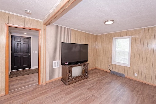 unfurnished living room featuring a textured ceiling, wood finished floors, ornamental molding, baseboards, and wooden walls