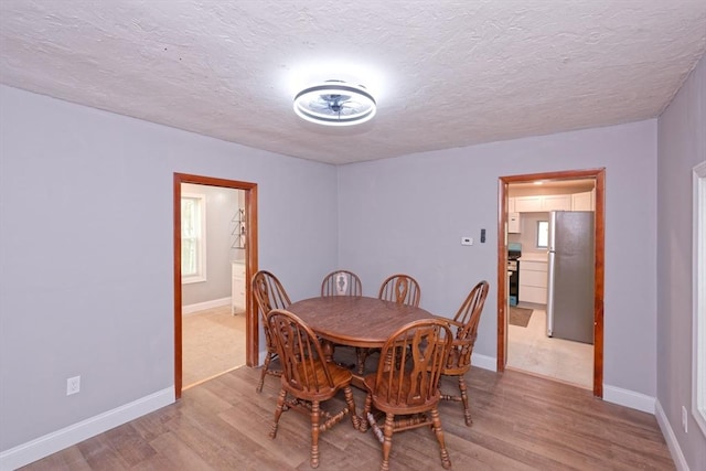 dining area with light wood-style floors, a textured ceiling, and baseboards