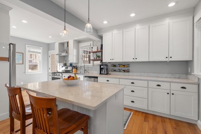 kitchen with open shelves, white cabinets, appliances with stainless steel finishes, a kitchen bar, and wall chimney range hood