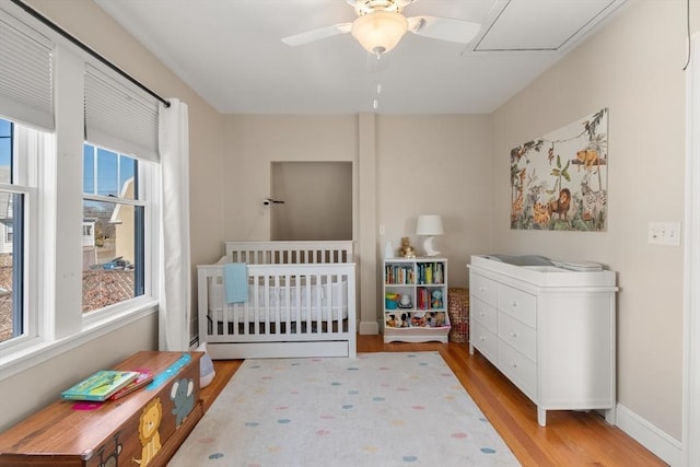 bedroom featuring a crib, a ceiling fan, baseboards, and wood finished floors