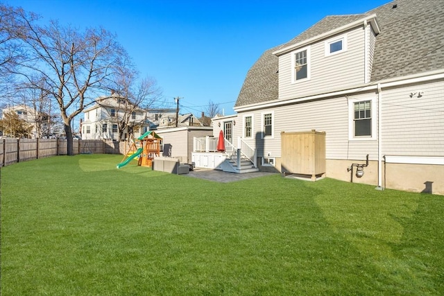 rear view of house with a playground, a lawn, a fenced backyard, and roof with shingles