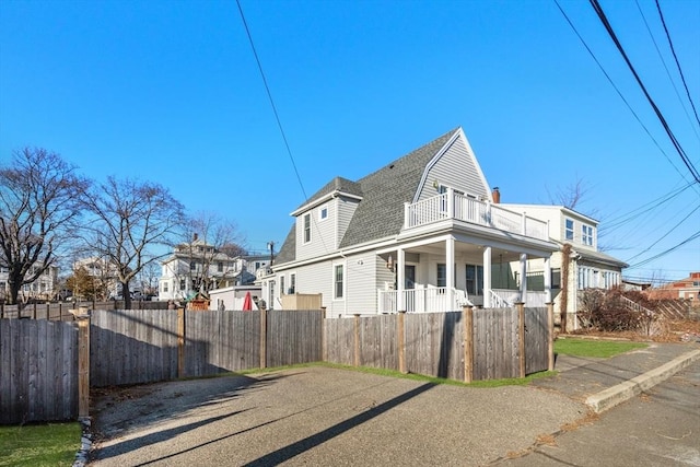 view of home's exterior with a fenced front yard, a gambrel roof, a balcony, and roof with shingles