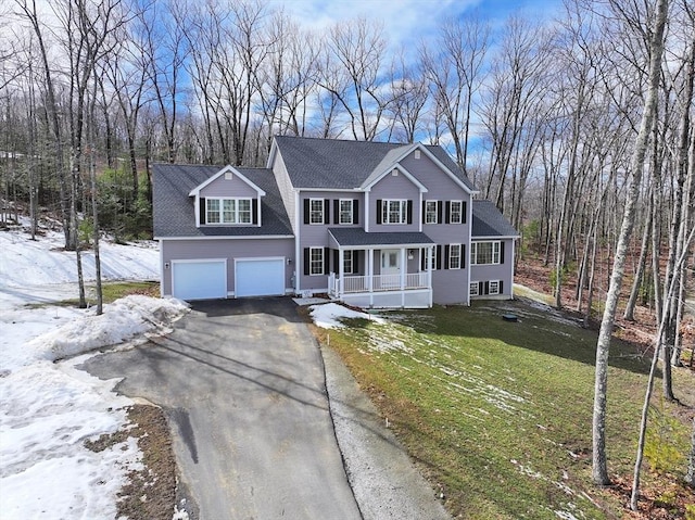 colonial-style house featuring a garage, covered porch, driveway, and a front lawn