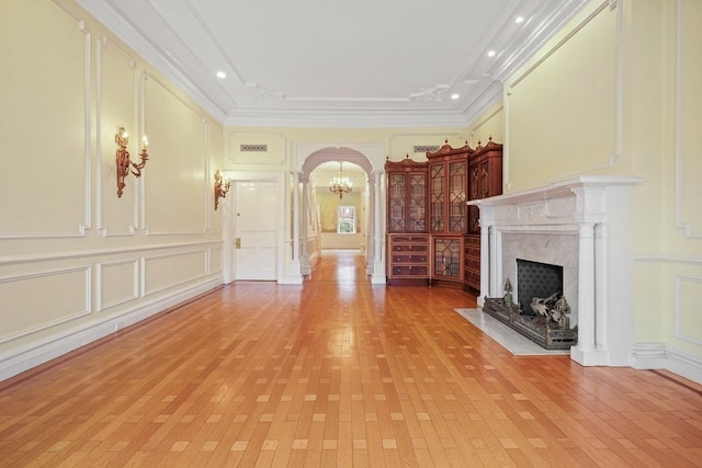 unfurnished living room with crown molding, a notable chandelier, light wood-type flooring, and a premium fireplace