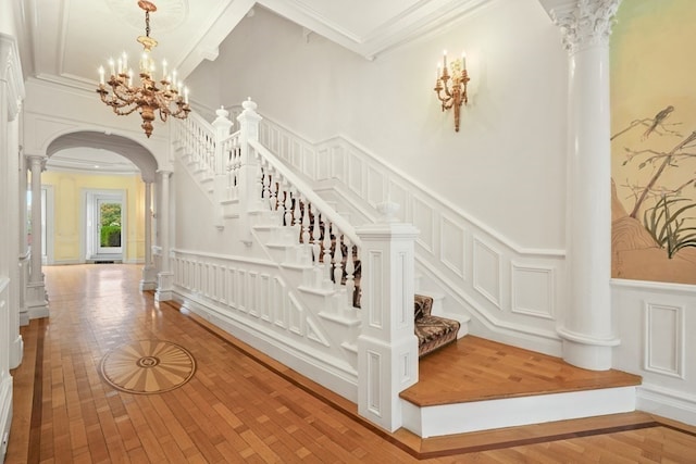 stairway with light hardwood / wood-style floors, a towering ceiling, a chandelier, crown molding, and ornate columns