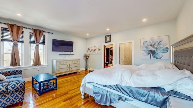 bedroom with wood finished floors, recessed lighting, baseboards, and a walk in closet