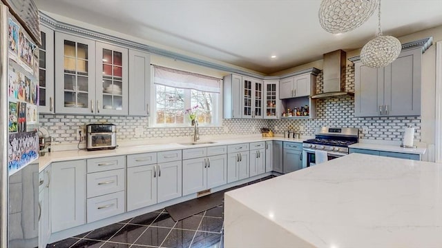 kitchen featuring stainless steel gas range oven, wall chimney exhaust hood, a sink, gray cabinetry, and light stone counters