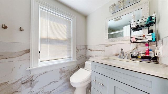 bathroom with tile walls, healthy amount of natural light, toilet, vanity, and wainscoting