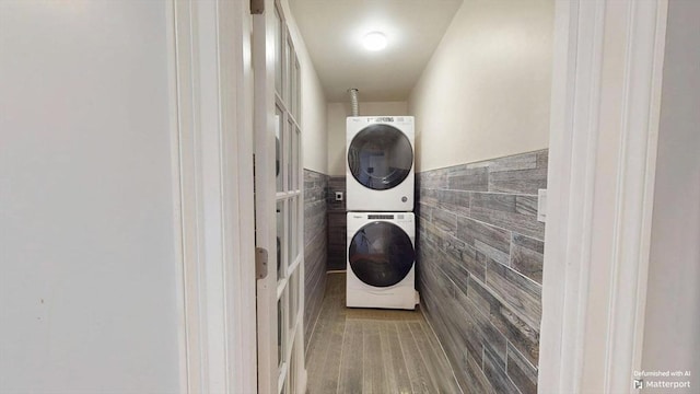 laundry room with stacked washer / dryer, tile walls, and a wainscoted wall