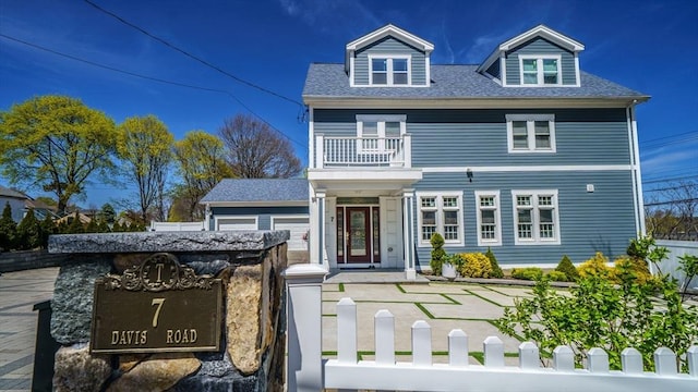 view of front of house featuring a balcony, a fenced front yard, and a shingled roof