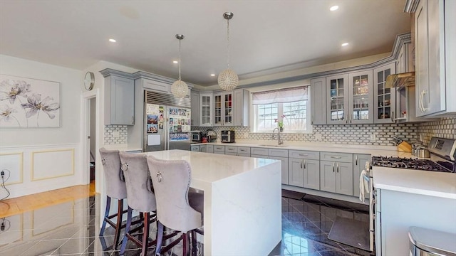 kitchen featuring stainless steel appliances, gray cabinetry, a sink, decorative backsplash, and a kitchen breakfast bar