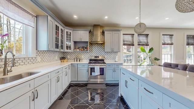 kitchen featuring stainless steel range with gas cooktop, wall chimney exhaust hood, granite tiled floors, a sink, and tasteful backsplash