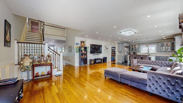 living room with stairway, light wood-style flooring, a wainscoted wall, recessed lighting, and a decorative wall